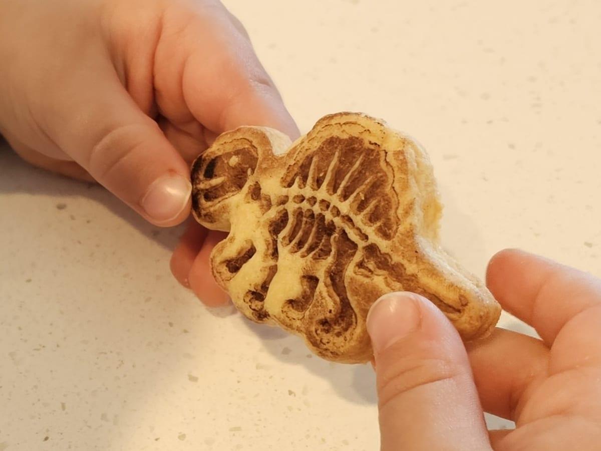 A child's hands holding a baked dinosaur fossil biscuit with the skeleton embossed into it